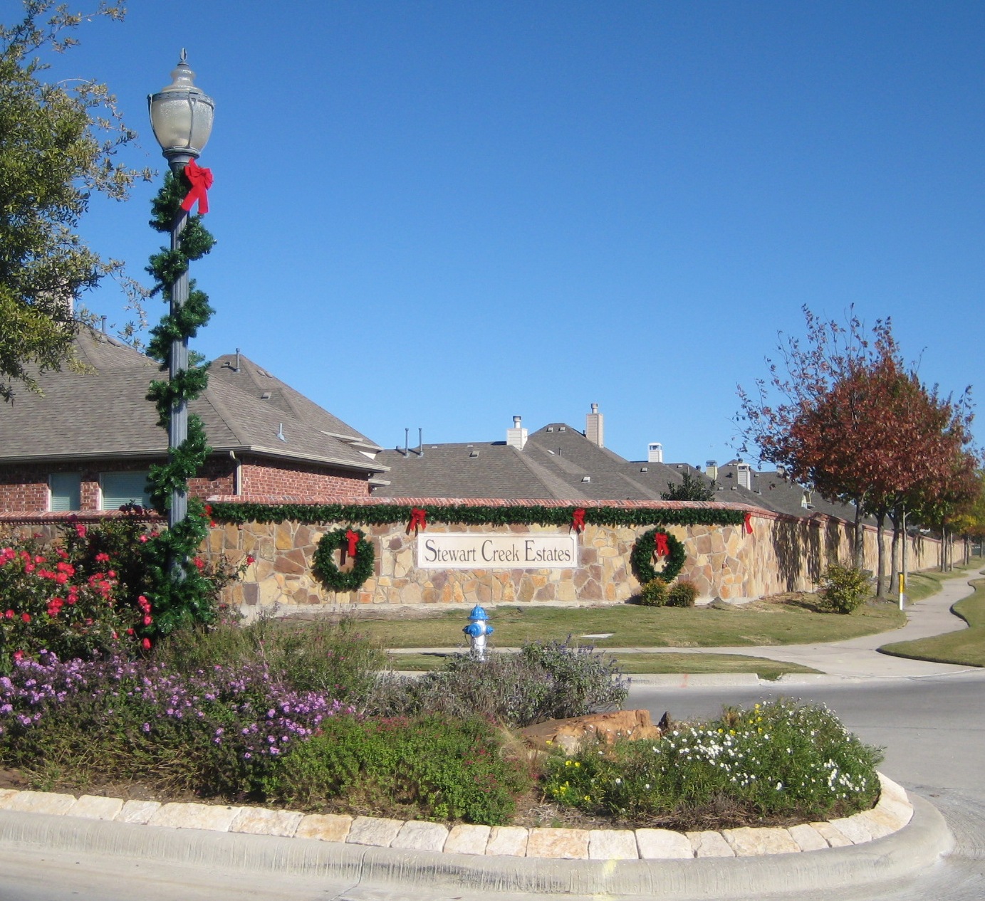 Stewart Creek Estates stone entrance wall decorated with garland, wreaths and red bows beside a garland-wrapped lamp post.