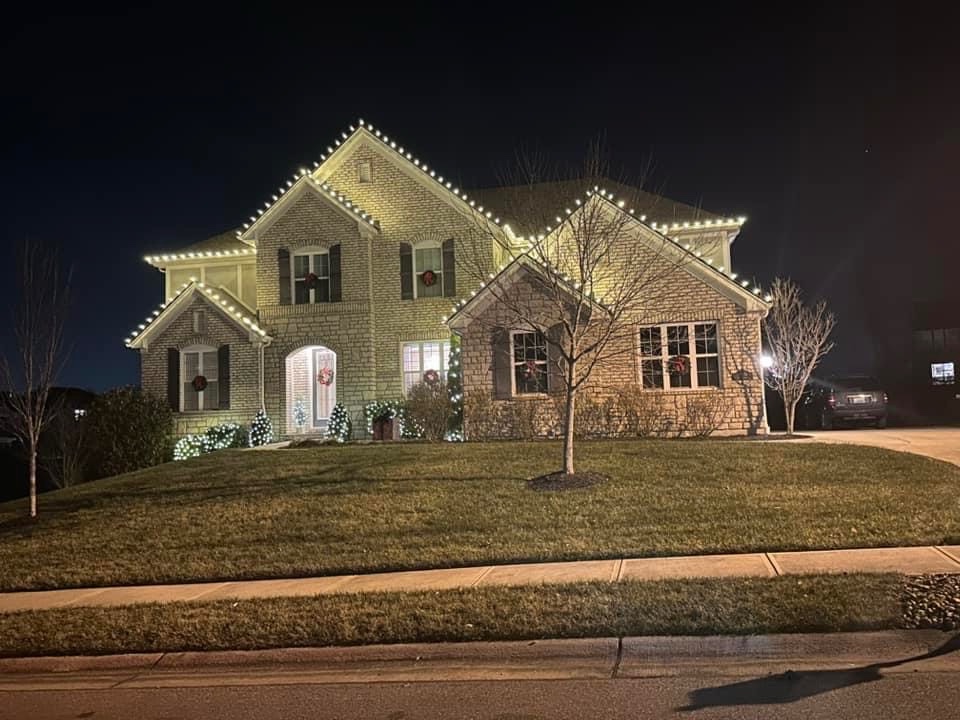 Warm white bulbs outline several brick roof peaks, with wreaths at windows and lights on front shrubs.