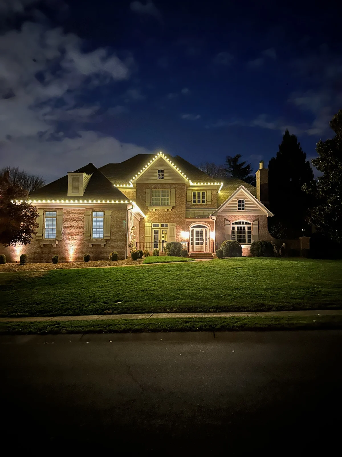 Warm white lights following a brick home’s roof peaks